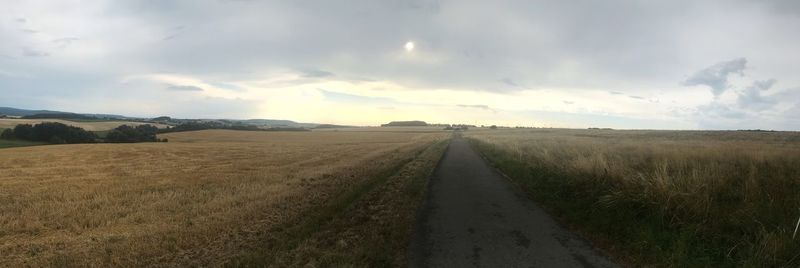 Empty road amidst field against sky