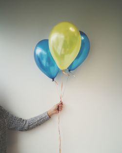 Close-up of hand holding balloons against white background