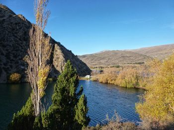Scenic view of river by mountains against clear blue sky