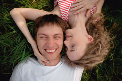 A man and a woman lie on the grass head to head and smile