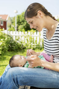 Smiling woman looking at baby while sitting at yard