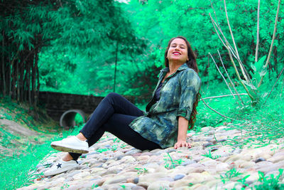 Portrait of young woman smiling while sitting against trees at park