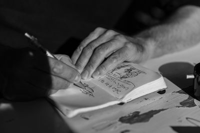 Close-up of man sketching in book on table