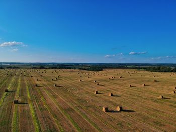 Hay bales on field against blue sky