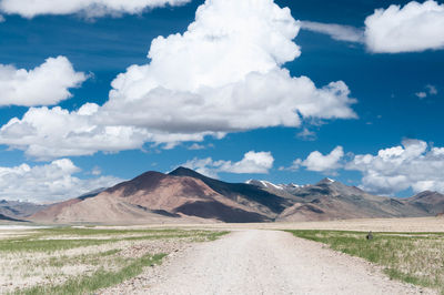 Scenic view of dirt road by mountains against sky