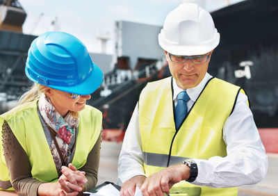 Engineer checking time in wristwatch standing by colleague at dock
