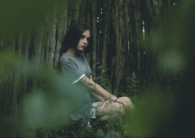 Portrait of young woman sitting by tree in forest