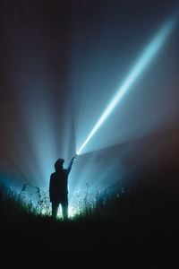 Man with illuminated flash light standing on field against sky at night