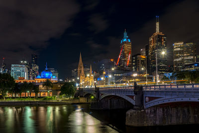 Illuminated bridge over river against buildings at night