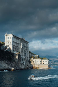 Buildings in sea against cloudy sky