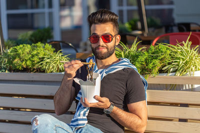 Young man holding drink sitting outdoors