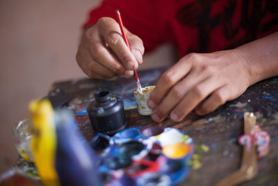 Close-up of hand holding painting brush at messy table