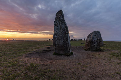 Rock formations on field against sky during sunset