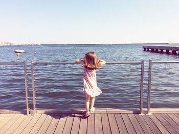 Rear view of girl standing on pier by sea