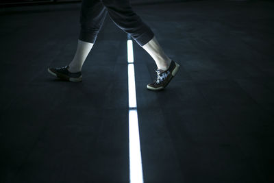 Low section of woman walking on illuminated footpath