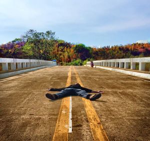 Man lying on road in city against sky