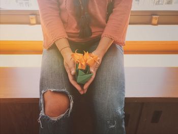 Midsection of woman holding paper flower while sitting on table