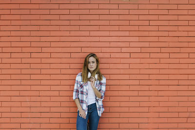 Portrait of young woman standing against brick wall