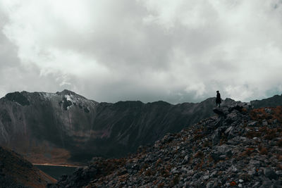 Low angle view of person standing on cliff against sky