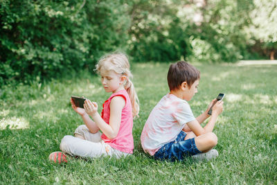 Cute kids using smart phone sitting at park