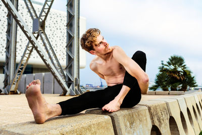 Full length of shirtless man sitting against sky