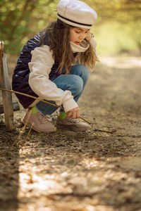 Little girl paints draws on ground with stick in open air in spring blooming fairytale park