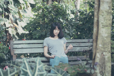 Young woman sitting on bench against trees