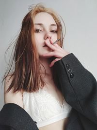 Portrait of beautiful young woman smoking cigarette against wall