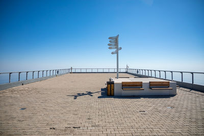 Street light on footpath by sea against clear blue sky