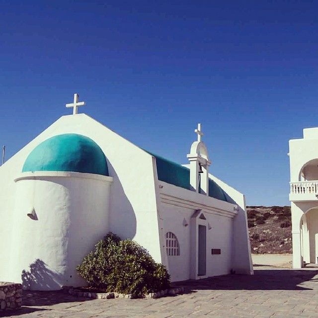 architecture, building exterior, built structure, blue, clear sky, religion, place of worship, church, spirituality, copy space, dome, cross, low angle view, sunlight, house, tree, day, outdoors