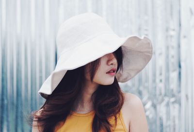 Close-up of young woman wearing hat standing against wall