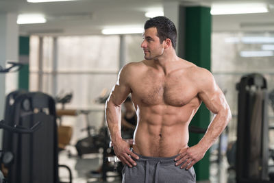 Shirtless muscular man with hands on hip standing in gym