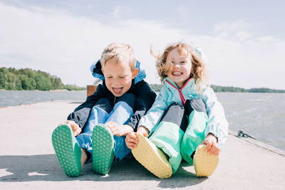 Brother and sister sat at the beach laughing together on a windy day