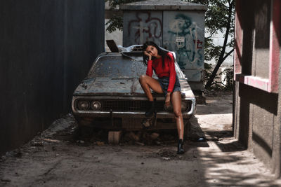 Full length of woman sitting on abandoned car