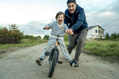 Father teaching son to ride bicycle on road