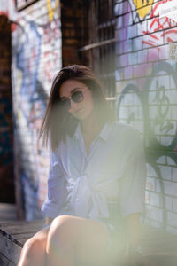 Portrait of young woman sitting on seat against graffiti wall