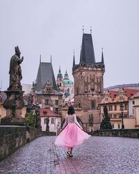 Rear view of woman walking on bridge against buildings in city