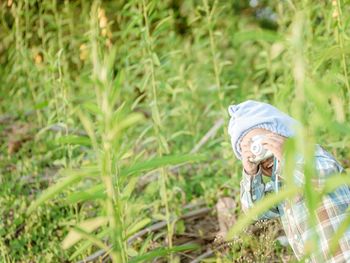Girl holding toy camera amidst plants