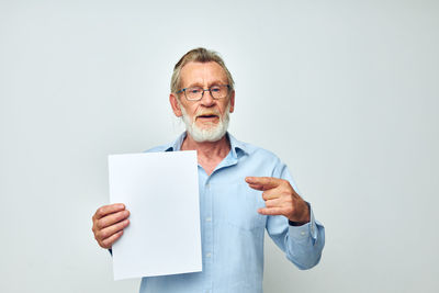 Portrait of man holding paper while standing against white background