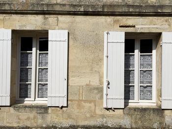 Saint emilion. stone shabby wall with two windows and wooden opened shutters. vintage lace curtains