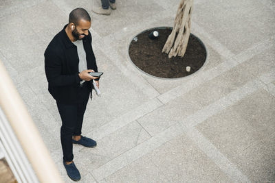 High angle view of happy male entrepreneur using phone while standing outside office