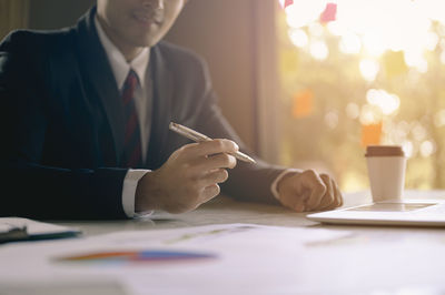 Midsection of businessman holding pen while sitting at office