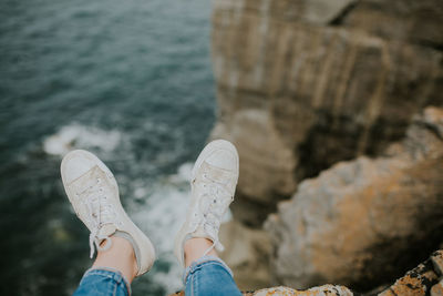 Low section of person sitting on cliff against sea