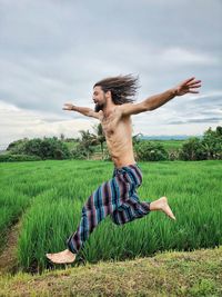 Shirtless man running on field against sky