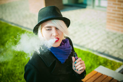 Young woman smoking while standing by built structure
