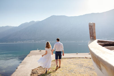 Rear view of couple walking on pier against mountains