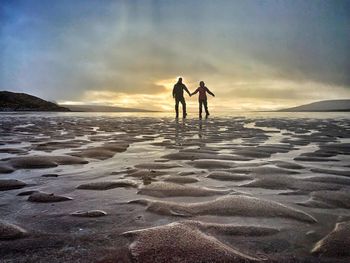 Silhouette friends standing on beach against sky during sunset