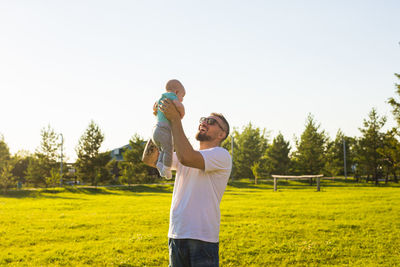 Father and son on grass against sky