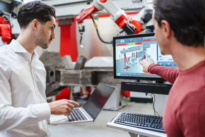 Engineer explaining colleague holding laptop at robot factory