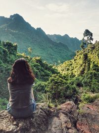 Rear view of woman sitting on mountain in forest
